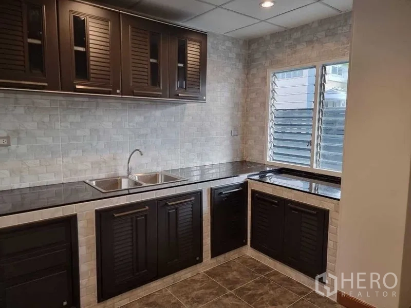 独立式住宅 出租在Mueang Nonthaburi, Nonthaburi - L形厨房，深色橱柜、黑色台面、瓷砖墙面与百叶窗。