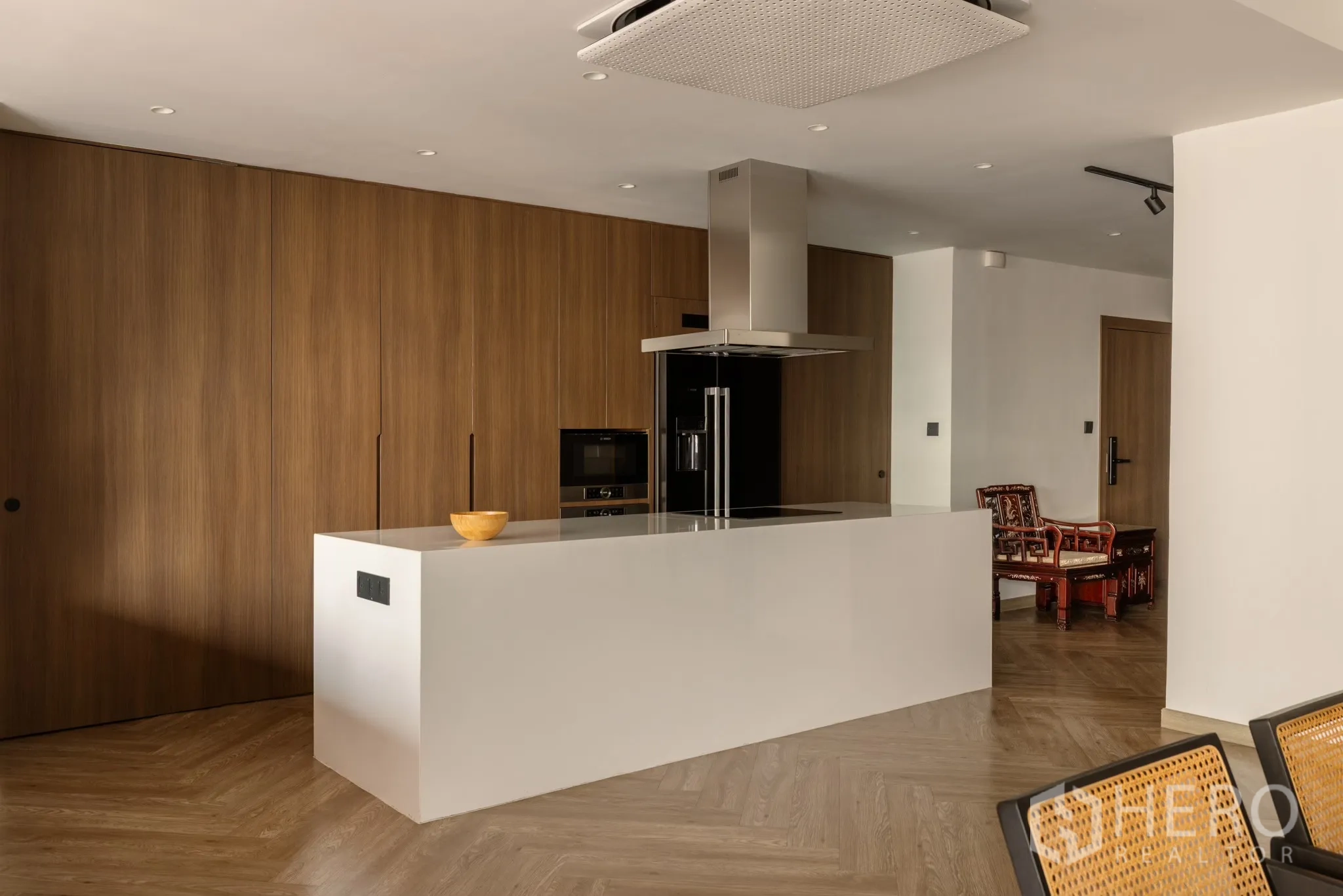 Condominium for sale in Khlong Toei, Bangkok - Open kitchen with sleek island, built‑in oven and fridge against a wall of warm wood cabinetry and herringbone floors.