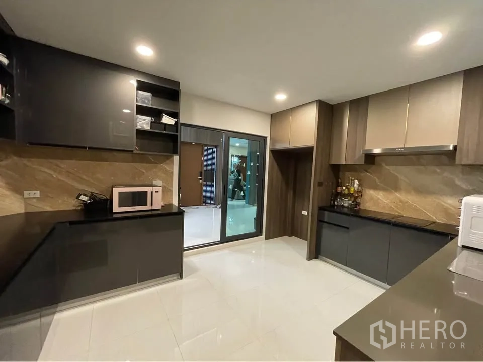 บ้านเดี่ยว for rent or sale in Bang Phli, Samut Prakan - ครัวปิดตู้สีเข้ม ผนังลายหิน และเครื่องดูดควัน