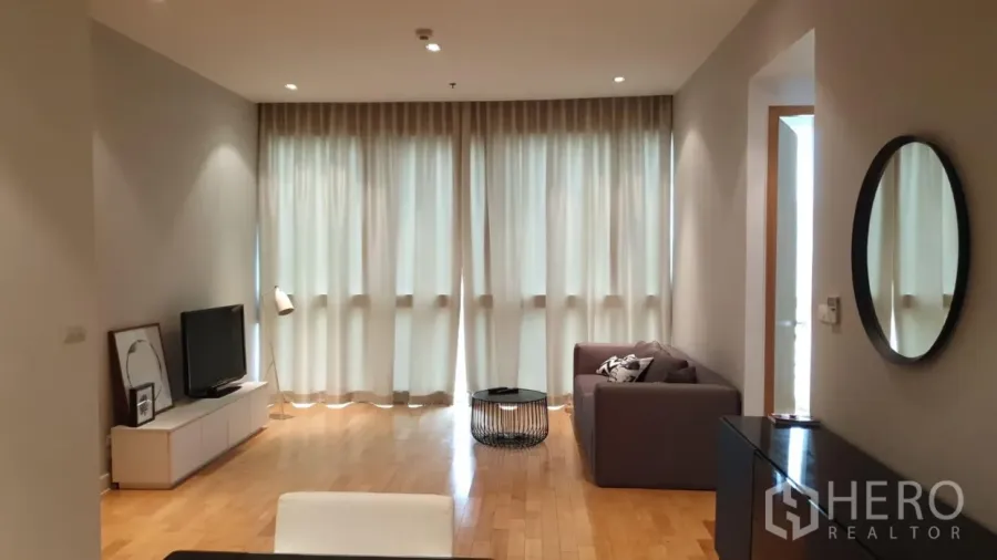 Condominium for rent or sale in Khlong Toei, Bangkok - Bright living room with floor-to-ceiling curtains, TV console, and warm wood flooring.