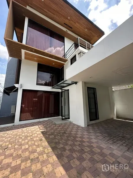 Home Office for rent in Watthana, Bangkok - Front facade with covered carport, brick driveway, large windows and warm wood soffit.