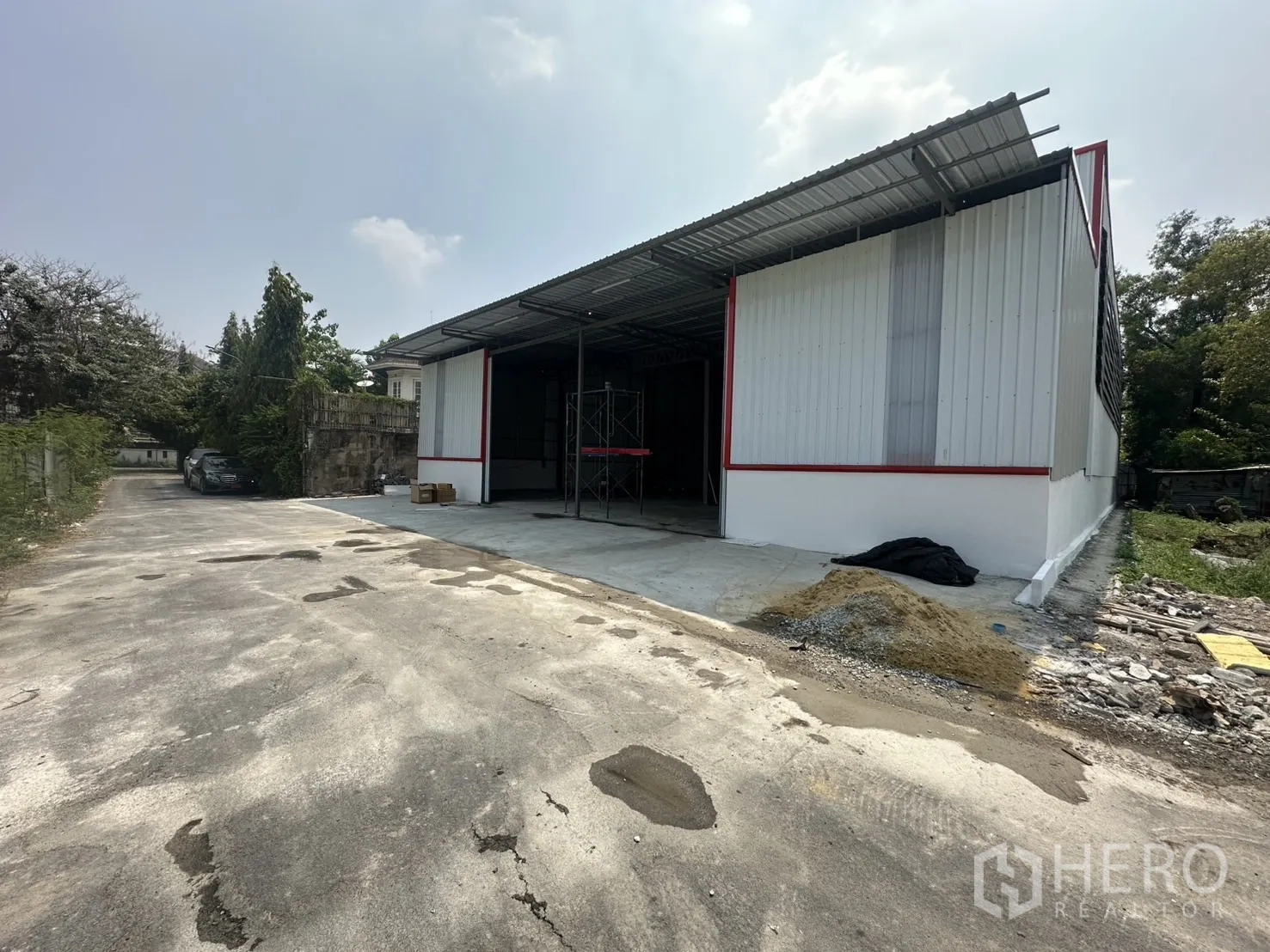 Warehouse for rent in Bang Kapi, Bangkok - Side view of warehouse with covered loading bay, concrete yard and driveway access, surrounded by greenery.