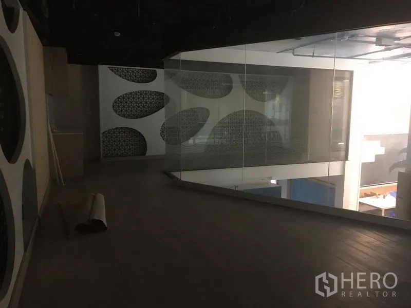 零售空间 出租在Khlong Toei, Bangkok - 夹层空间配玻璃栏板，俯瞰开放式楼层与抽象墙面装饰。