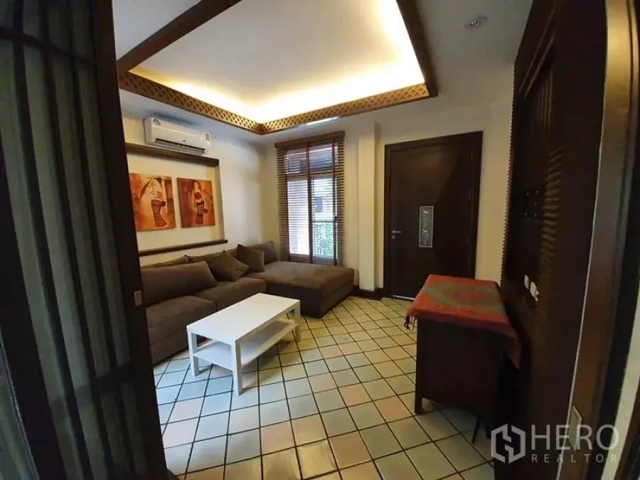 Detached House for rent in Wang Thonglang, Bangkok - Cozy living room with tiled floor, L-shaped sofa, cove lighting, artwork and window blinds.