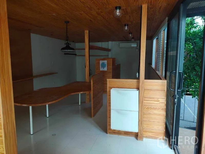 办公空间 出租在Khlong Toei, Bangkok - 紧凑办公套间，推拉玻璃门，弧形木桌与木质墙面，外部绿意。