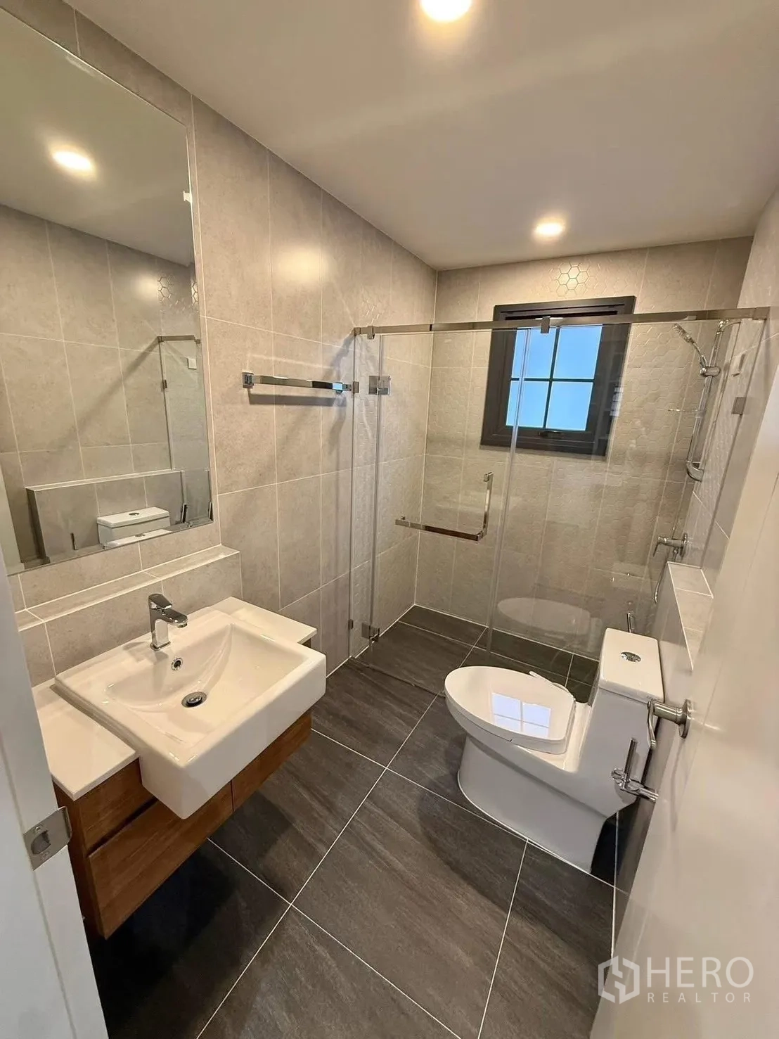 Detached House for rent in Bang Phli, Samut Prakan - Modern bathroom with glass-enclosed shower, wall-hung sink, grey tiles and a window.