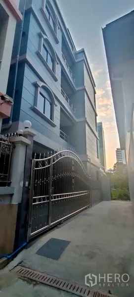 带办公室的家 出租在Pathum Wan, Bangkok - 傍晚视角的蓝灰色家庭办公楼立面与大门入口。