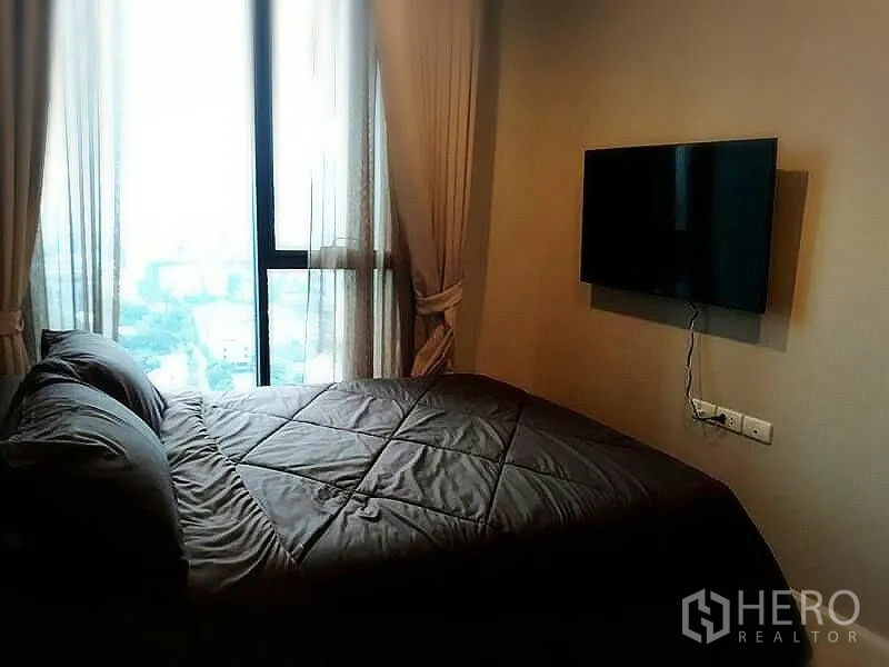 Condominium for rent or sale in Huai Khwang, Bangkok - Bedroom with wall-mounted TV and floor-to-ceiling window with city outlook.