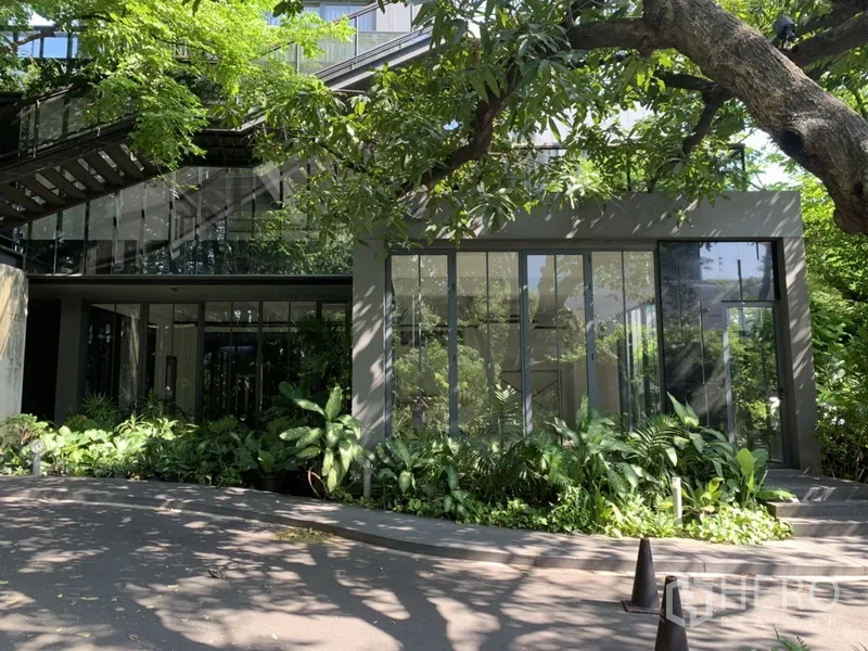 Office Space for rent in Khlong Toei, Bangkok - Modern low-rise office exterior with tall glass windows, shaded driveway and dense landscaping.