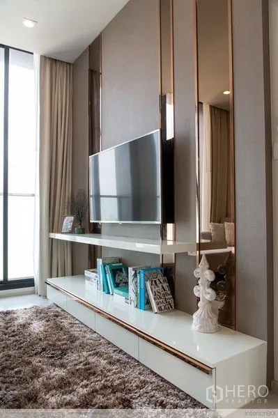 Condominium for rent in Pathum Wan, Bangkok - TV console with floating shelf, decor books and plush carpet next to a tall window.