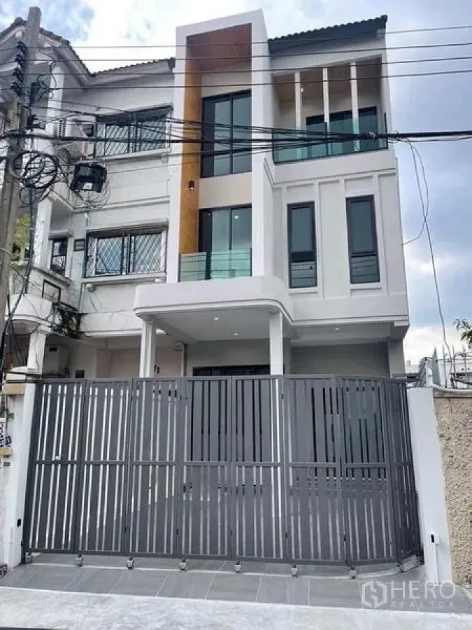 Townhouse for sale in Watthana, Bangkok - Contemporary townhouse exterior featuring large windows and a secure front gate.