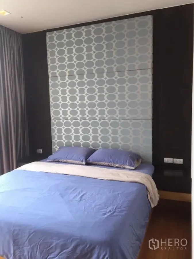 คอนโด ให้เช่าหรือขายในWatthana, Bangkok - ห้องนอนหลักพร้อมผนังหัวเตียงลวดลายบุผ้า ชุดเครื่องนอนสีน้ำเงิน และผ้าม่านสูงจรดเพดาน