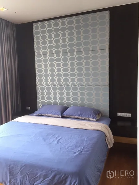 คอนโด ให้เช่าหรือขายในWatthana, Bangkok - ห้องนอนหลักพร้อมผนังหัวเตียงลวดลายบุผ้า ชุดเครื่องนอนสีน้ำเงิน และผ้าม่านสูงจรดเพดาน