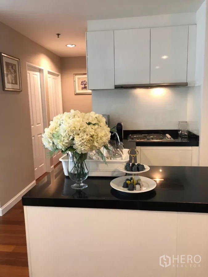 Condominium for rent in Huai Khwang, Bangkok - Kitchen island with glossy black surface, storage and coffee machine beside the hallway.