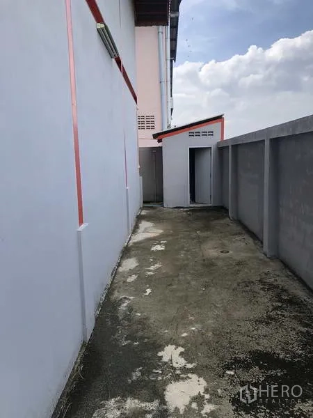 货栈 出租在Nonthaburi - 仓库侧边服务通道，混凝土地面、围墙及小型附属用房。