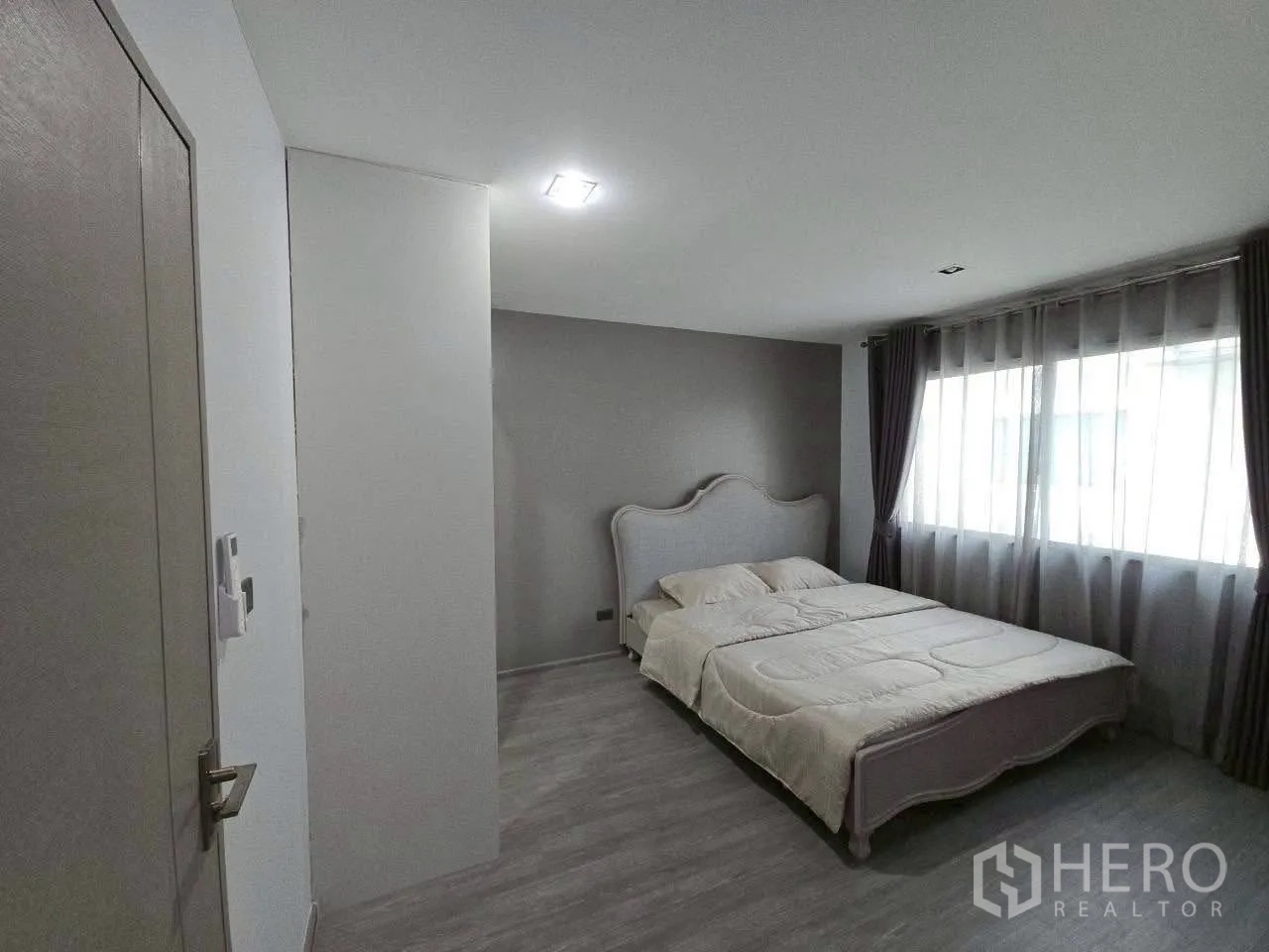 ทาวน์เฮาส์ ให้เช่าหรือขายในLat Phrao, Bangkok - ห้องนอนโทนเทา เตียงคู่ ผนังหัวเตียง และหน้าต่างบานใหญ่พร้อมผ้าม่าน