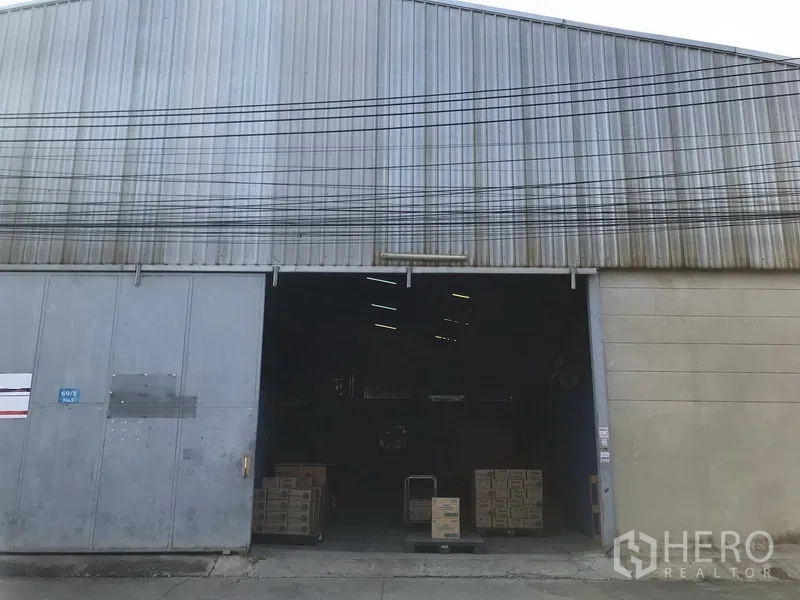 货栈 出租在Bang Phli, Samut Prakan - 工业仓库正面，宽大的金属推拉门开启，装卸区可见堆放的纸箱。