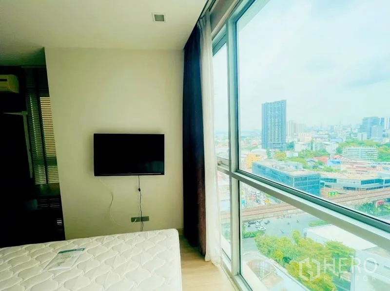 Condominium for rent - Bedroom with wall-mounted TV and large window overlooking the Bangkok skyline.
