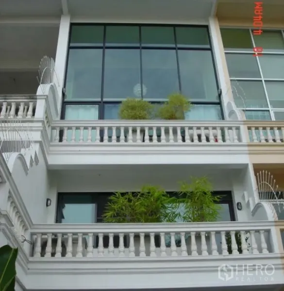 联排别墅 出售在Phra Khanong, Bangkok - 多层联排别墅外立面，落地玻璃与双阳台，摆放竹植，靠近BTS Punnawithi