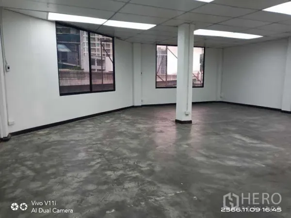 Office Space for rent in Bang Na, Bangkok - Large open-plan office with concrete floor, central column and windows facing nearby buildings.