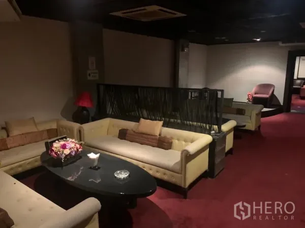 零售空间 出租在Bang Rak, Bangkok - 铺地毯的休息区，米色沙发、椭圆茶几与柔光照明。