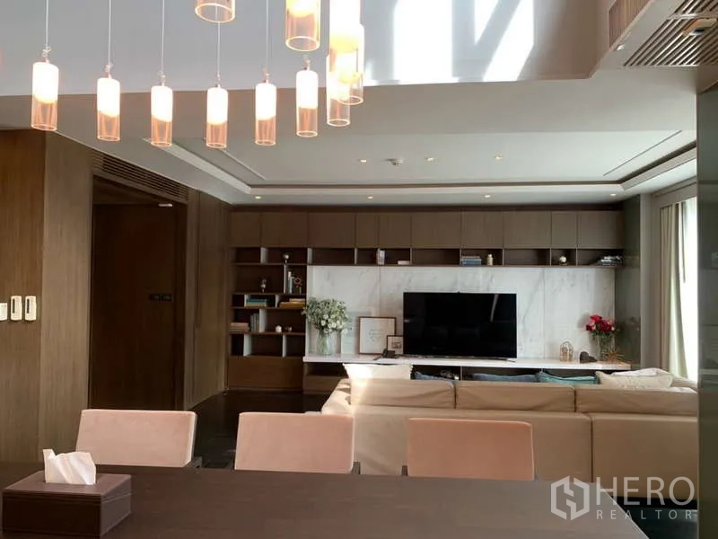 Condominium for rent in Khlong Toei, Bangkok - Bright living room with marble TV wall, built-in shelving and a beige sofa under pendant lights.