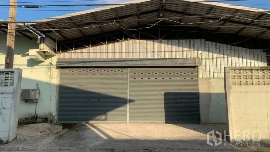 Warehouse for rent in Mueang Nakhon Pathom, Nakhon Pathom - Street-facing steel-clad warehouse facade with twin roller shutter doors and a concrete driveway.