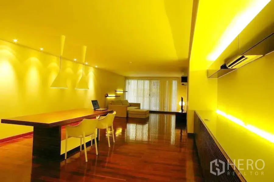 Condominium for rent in Watthana, Bangkok - Open-plan living and dining area with pendant lights, long wooden table, glossy wood floors and floor-to-ceiling blinds.