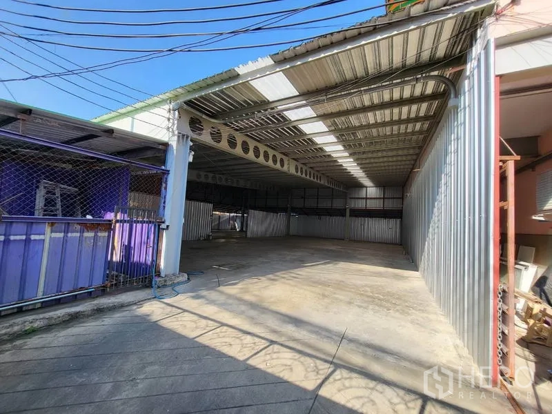 Warehouse for rent in Din Daeng, Bangkok - Front yard with sliding gate leading to a sheltered warehouse area and concrete apron.