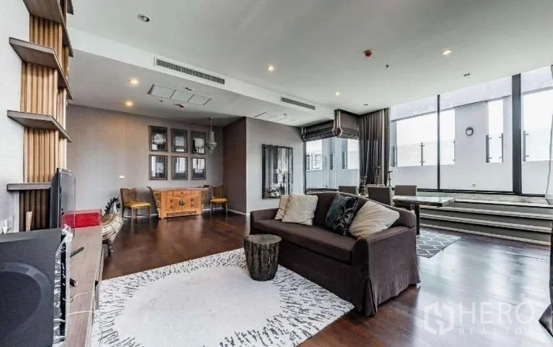 Condominium for rent - Living area with sofa, area rug and media cabinet beside tall windows.