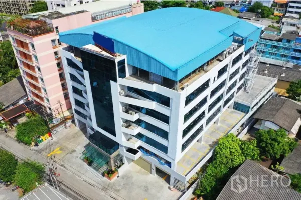 办公空间 出租在Khlong Toei, Bangkok - 曼谷空堤区蓝色屋顶的现代化中高层办公楼鸟瞰图，配有停车位。