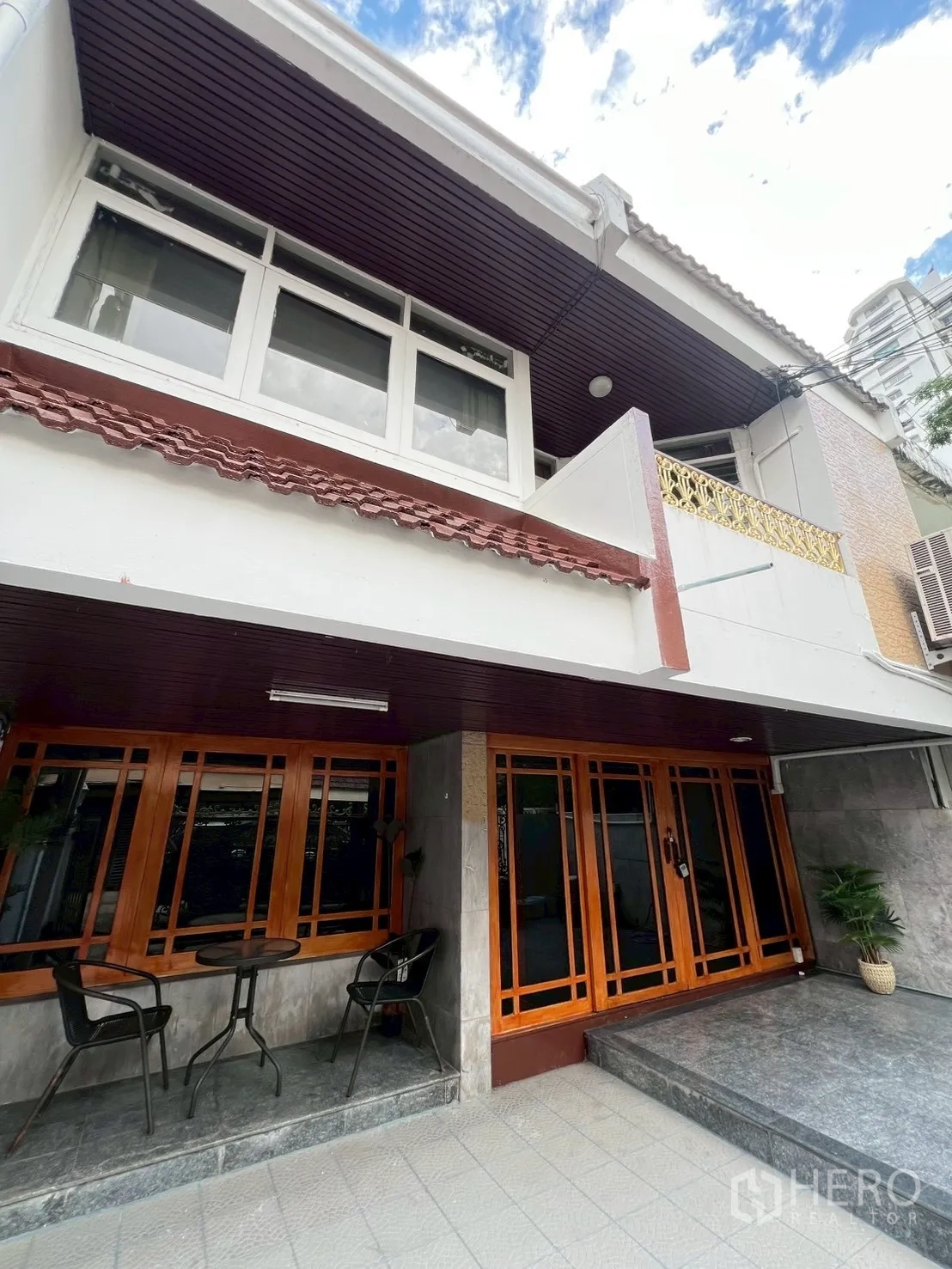 Home Office for rent in Watthana, Bangkok - Angled exterior showing tiled patio, café set and large wooden windows.
