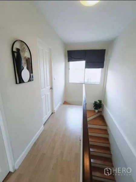 联排别墅 出租在Bang Kapi, Bangkok - 明亮的楼上走廊，挂镜、窗户与木地板通往卧室。