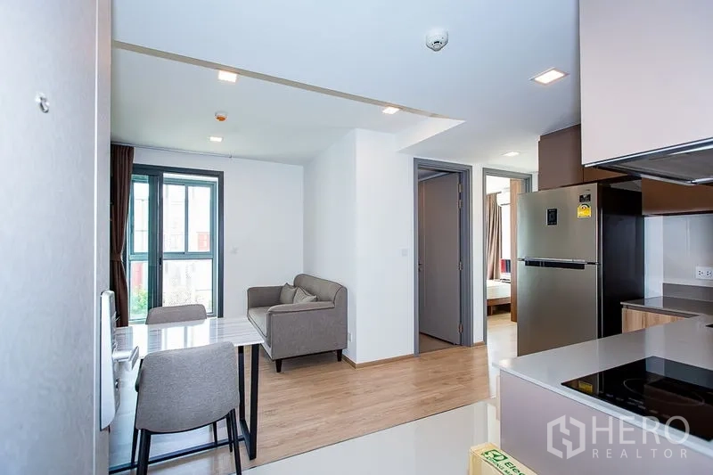 คอนโด ให้เช่าในWatthana, Bangkok - พื้นที่นั่งเล่นโปร่งสว่างพร้อมโซฟา โต๊ะทานอาหาร และครัวบิลต์อินพร้อมตู้เย็นและเตา พื้นไม้และหน้าต่างบานสูง