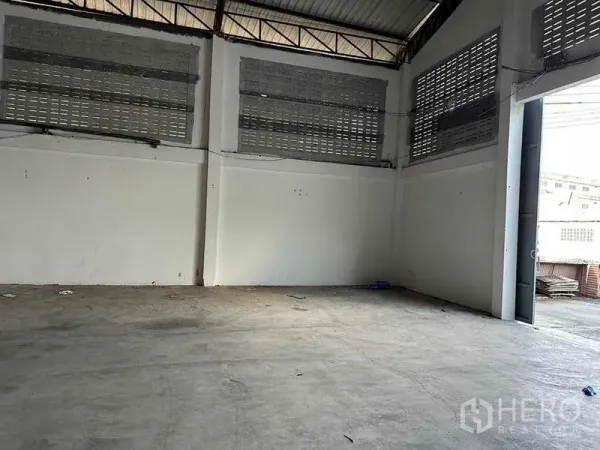 Warehouse for rent in Mueang Samut Sakhon, Samut Sakhon - Corner of the warehouse near the loading entrance showing tall walls, ventilation block windows and concrete floor opening to the driveway.