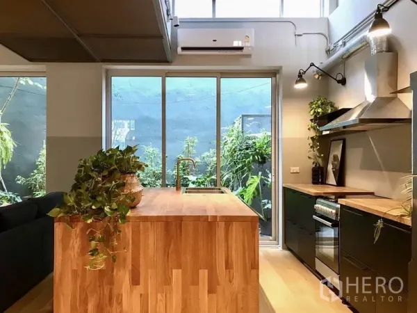 Townhouse for rent in Khlong Toei, Bangkok - Contemporary kitchen with wood island, black cabinetry and sliding doors to a small garden.