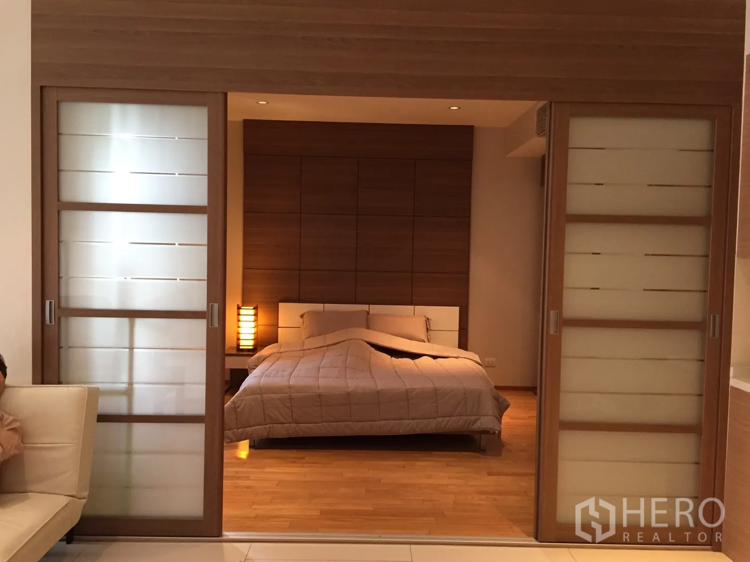公寓 出租或出售在Khlong Toei, Bangkok - 卧室木质背景墙，暖色灯光，磨砂玻璃推拉门。