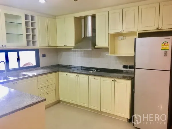 Condominium for rent in Watthana, Bangkok - Spacious U-shaped kitchen with cream cabinets, granite countertops, cooktop, hood and a window.