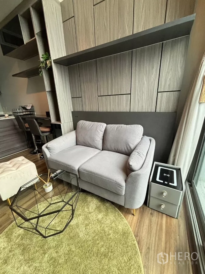 Condominium for rent or sale in Watthana, Bangkok - Close-up of gray loveseat and geometric glass coffee table against custom cabinets.