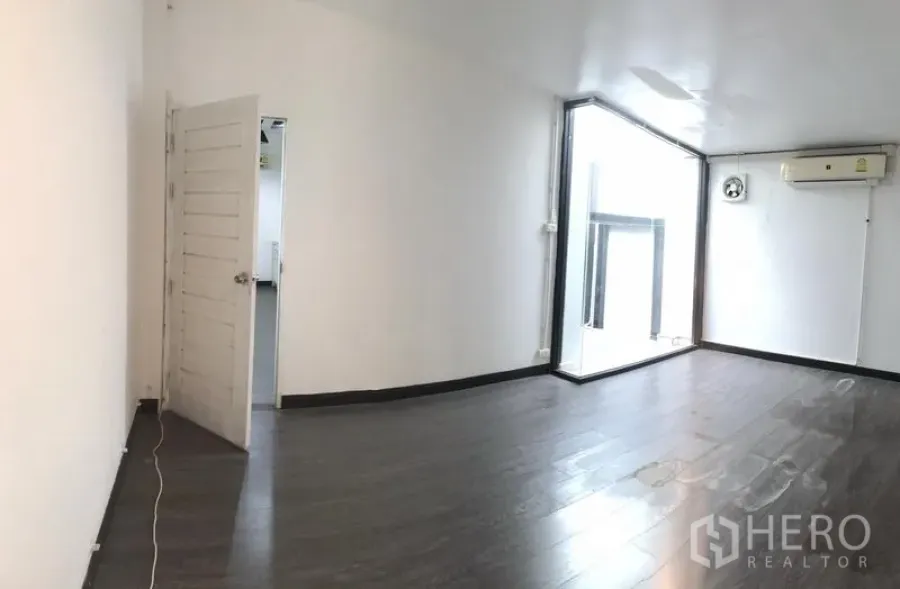 อาคารพาณิชย์ ให้เช่าในWatthana, Bangkok - ห้องโล่งพื้นไม้สีเข้ม ผนังขาว มุมกระจกพร้อมแอร์ และประตูเชื่อมพื้นที่ถัดไป