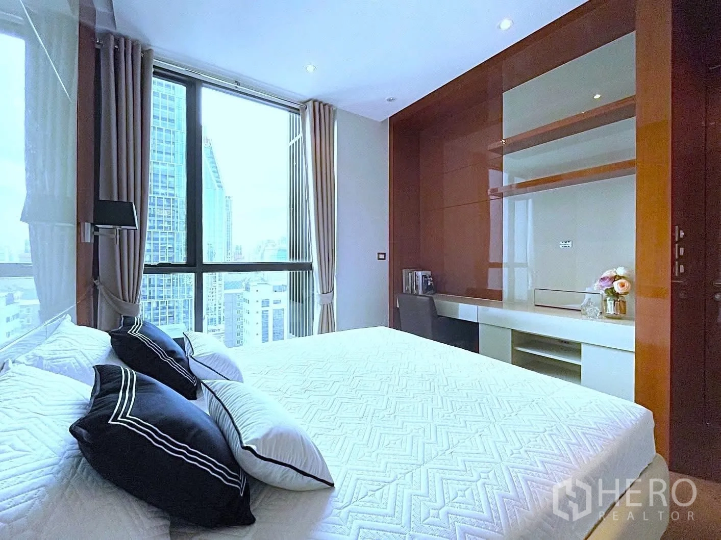Condominium for rent in Khlong Toei, Bangkok - Bright bedroom with floor-to-ceiling window, city skyline view, and built-in desk with shelving.