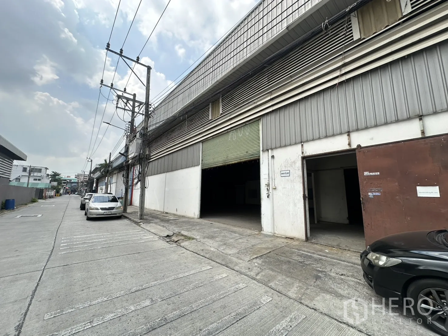 货栈 for rent in Suan Luang, Bangkok - 街道视角的工业仓库，绿色卷闸门与侧门，混凝土路面。