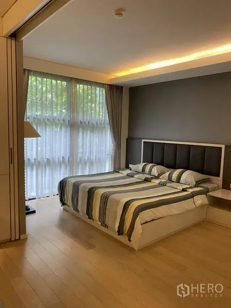 Condominium for rent in Watthana, Bangkok - Spacious bedroom with large bed, wood flooring, and full‑height windows dressed with sheer drapes.