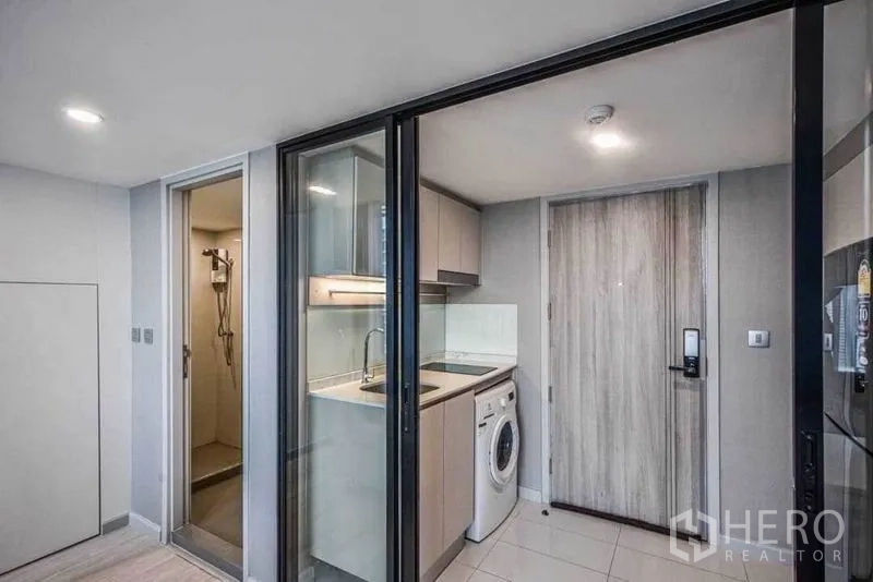 Condominium for rent in Sathon, Bangkok - Compact kitchen with sink, cabinets and washing machine behind sliding glass doors next to entry and shower room.