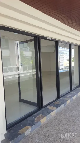 Office Space for rent in Khlong Toei, Bangkok - Modern glass storefront with black frames facing the corridor, showing the vacant office inside.
