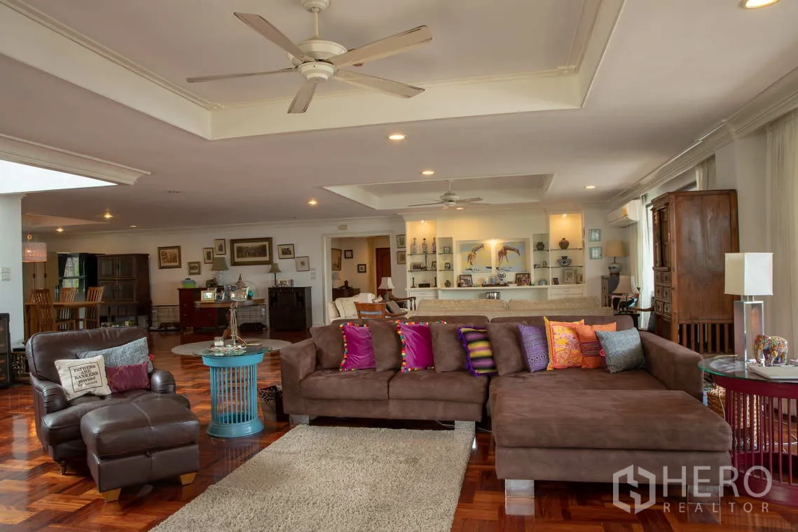 Apartment for rent in Khlong Toei, Bangkok - Large living room with sectional sofa, ceiling fans, and built-in shelving.