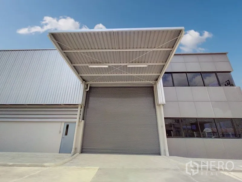 Factory for rent or sale in Samut Prakan - Covered loading bay with large roller shutter door at the industrial building.