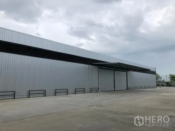 Warehouse for rent in Pathum Thani - Side view of corrugated metal warehouse with canopy-covered loading bay and wide driveway.
