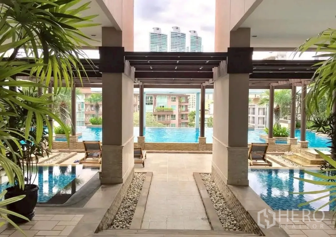 Condominium for rent in Khlong Toei, Bangkok - Covered walkway to a landscaped swimming pool with pergola and sun loungers.