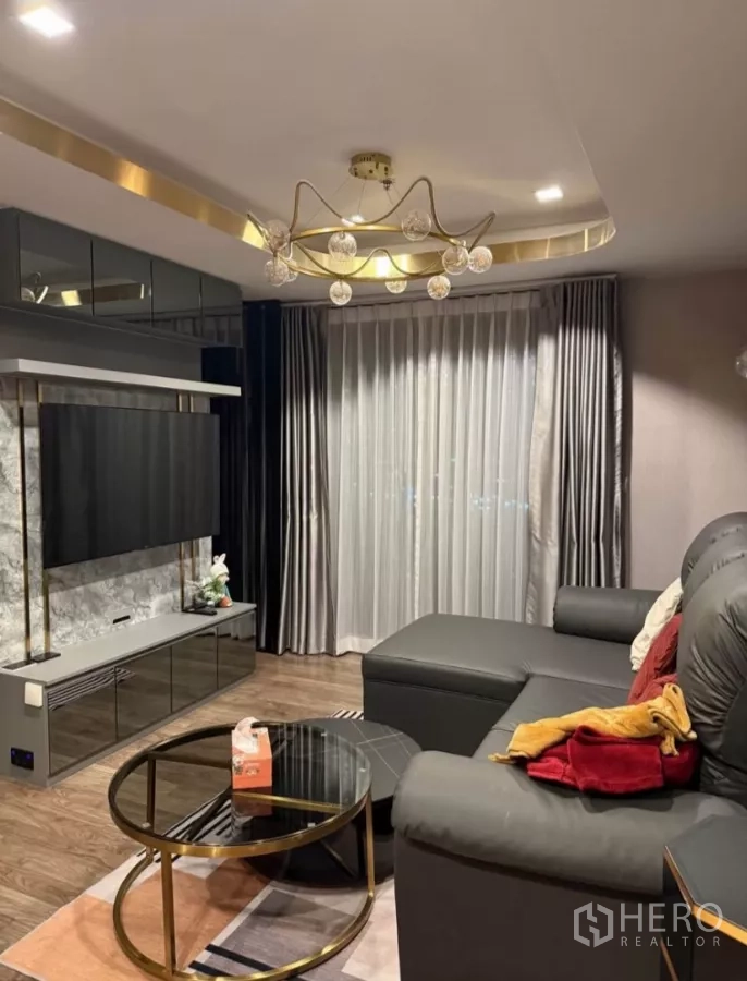 Condominium for rent in Chatuchak, Bangkok - Luxury living room with L-shaped leather sofa, mounted smart TV, gold chandelier, and floor-to-ceiling curtains.